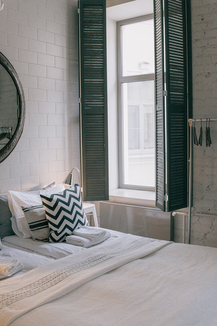 A cozy and stylish bedroom featuring modern decor and a sunlit window with shutter panels.